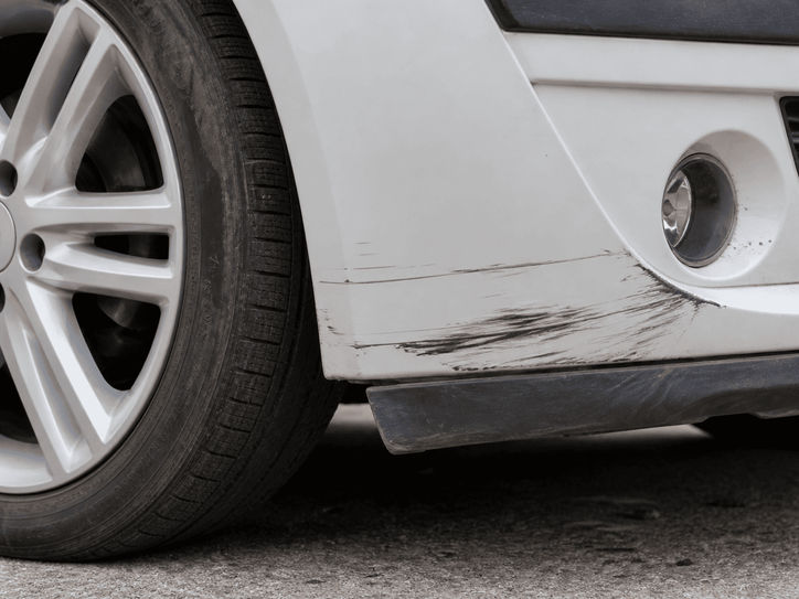 Scratched front bumper and wheel of a white car.