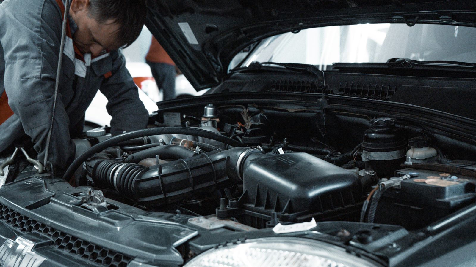 Mechanic inspecting a car engine in a repair shop.