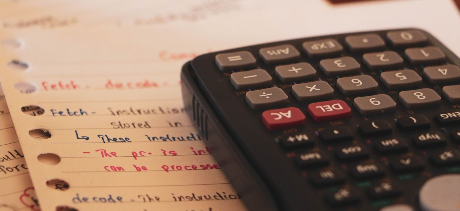 A black calculator on top of notebook pages filled with handwritten lines and calculations