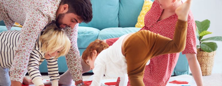 A family of Mum, Dad, and a young boy and girl playing Twister on their living room floor