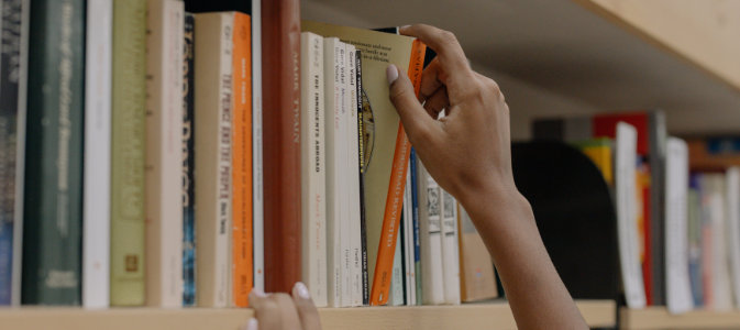 a person pulls a book from a bookshelf.