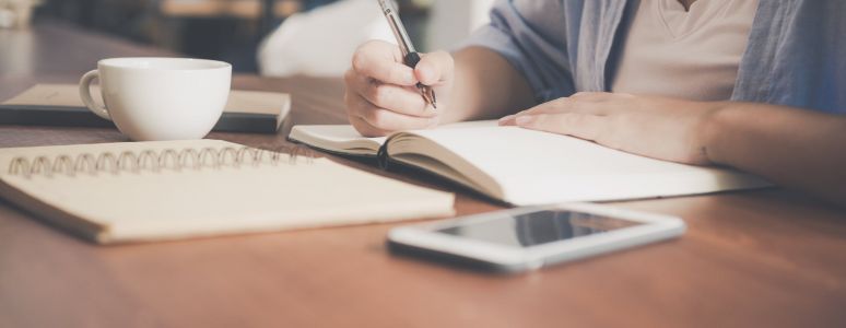 person writing at table with notebooks