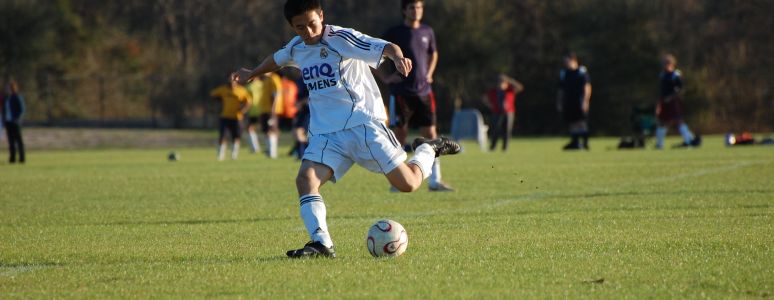 Young man kicking ball on grass pitch in football kit