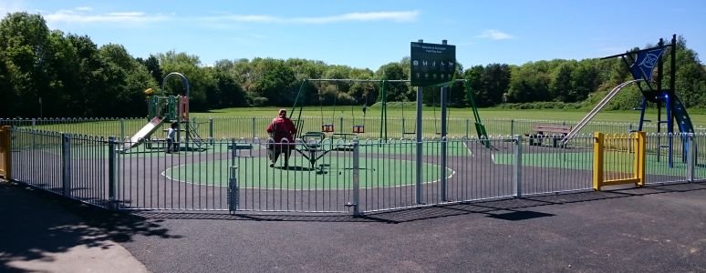 wide angle image showing whole of playground including swings, slide and climbing frame