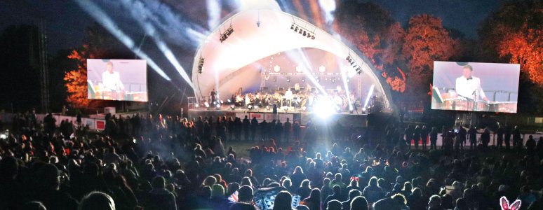 View of the half-circle shaped stage at Darley Park with big screens on each side. The background and the crowds in front are dark, and there are lights coming from the stage.