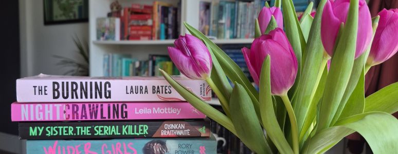 A pile of books next to a vase of pink tulips