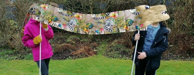 2 children holding up concertina dragon in garden