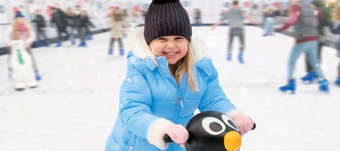 A little girl in a blue coat skates around the Cathedral Quarter Ice Rink with her penguin skate aid.