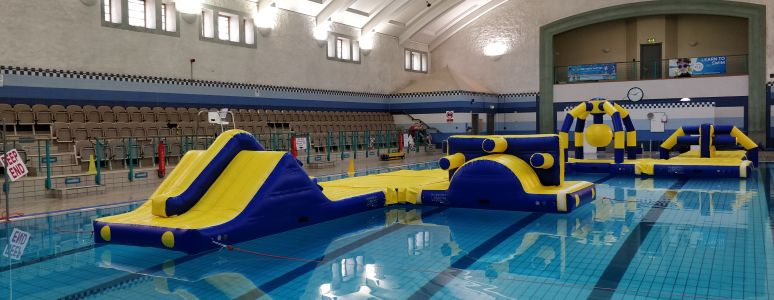 A large blue and yellow inflatable obstacle course with slides and slopes in a swimming pool
