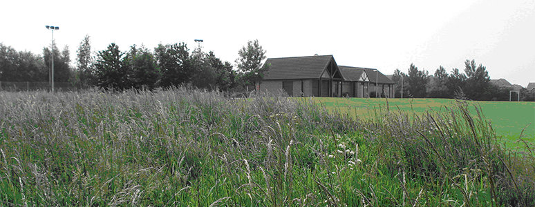 Image of chellaston community building in distance with grass and long grass in foreground