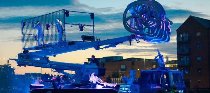 A giant light up blue face on a crane, with the sun-setting over the scene.