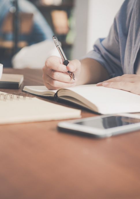 person writing at table with notebooks