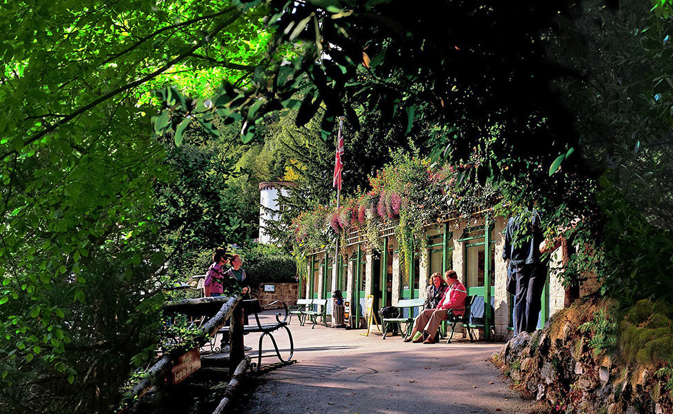 Exterior of the Tavern surrounded by foliage with people sitting relaxing outside