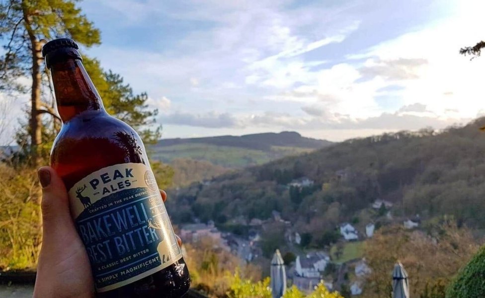 Someone holding up a beer bottle in front of scenic views of Matlock
