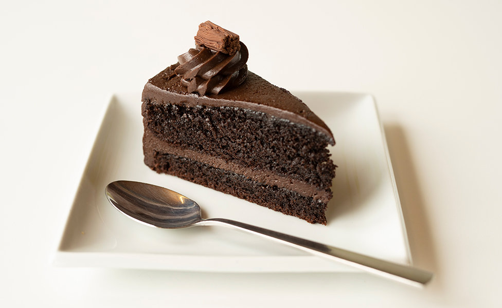 A slice of chocolate cake on a plate along side a spoon