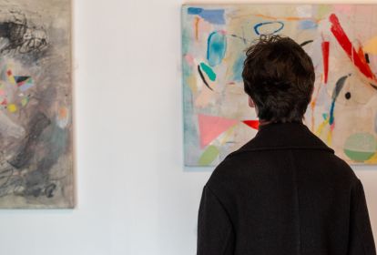 A man looking a bright abstract paintings hanging on a white wall