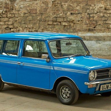 A vintage blue car in front of a brick wall