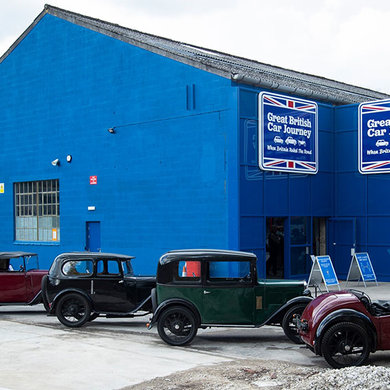 Four vintage cars in front of a large blue building