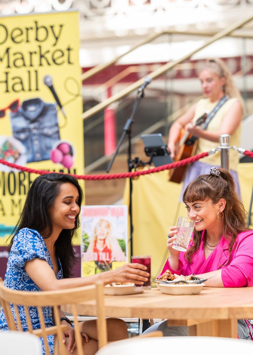 Two women enjoying a meal together at Derby Market Hall and listening to a live singer