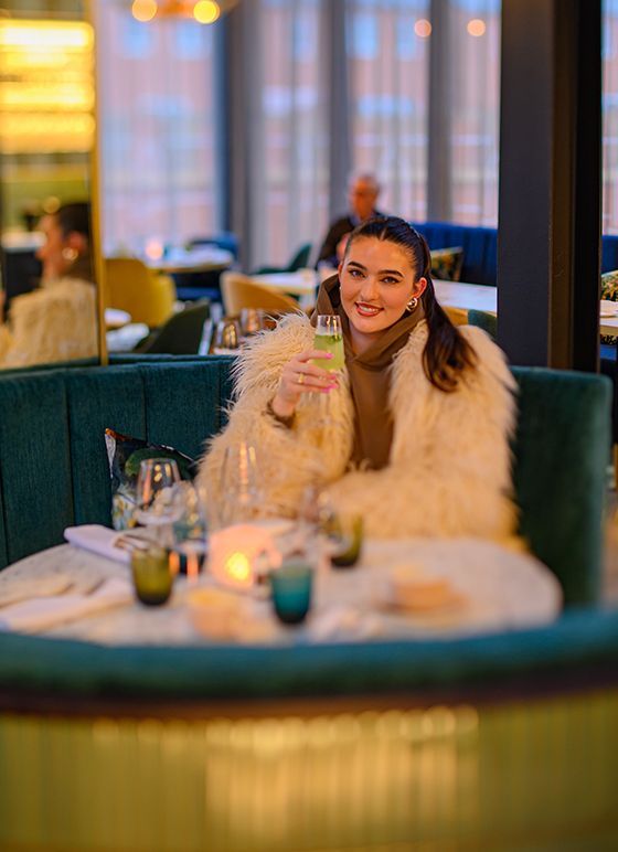 A woman sits at a table, smiling and enjoying a drink inside The Pepperpot in Derby