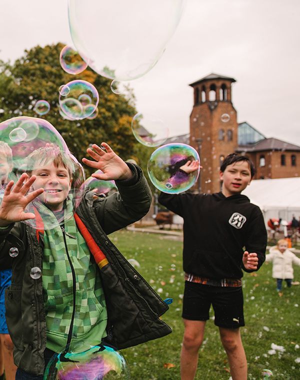A joyful group of children laughing and chasing colorful soap bubbles outside the Museum of Making