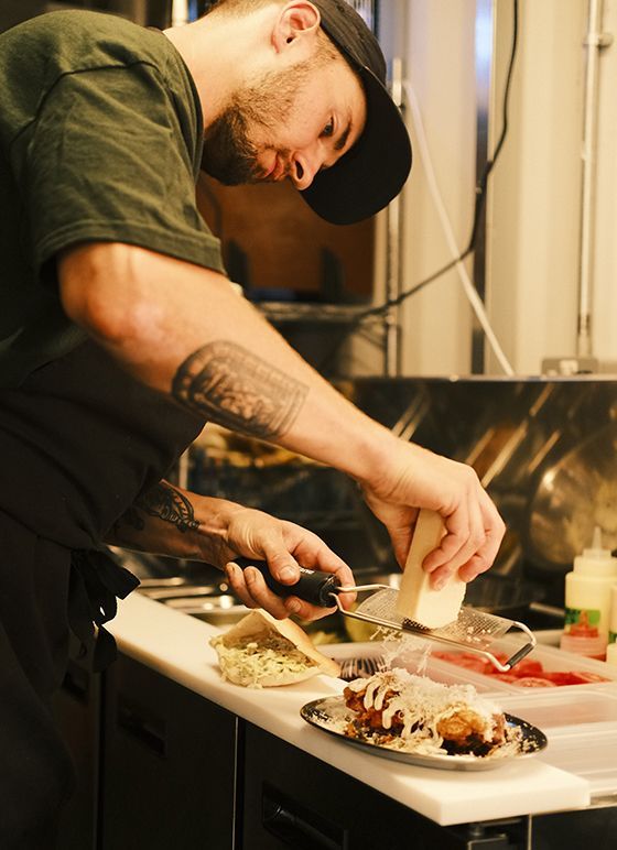 A man cooking at Bustler Derby, surrounded by fresh ingredients and kitchen tools.