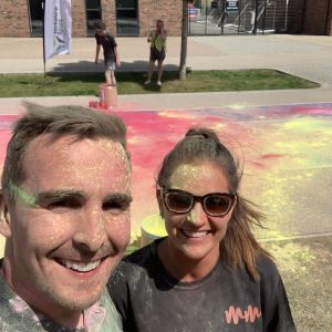 A couple smiling for a photo with colourful powder on their faces