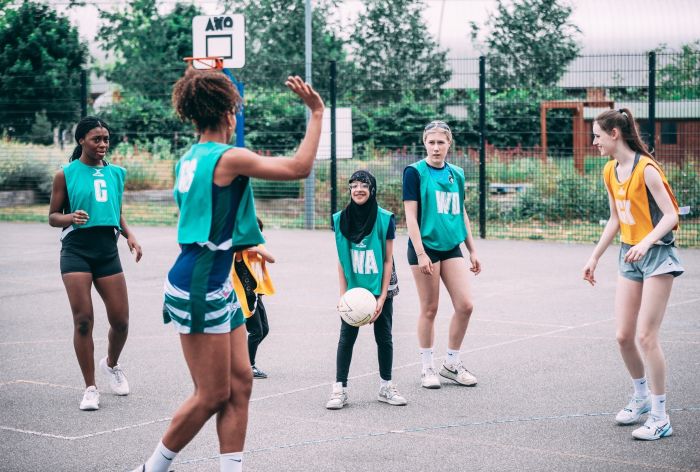 A diverse group of young women playing netball on an outdoor court