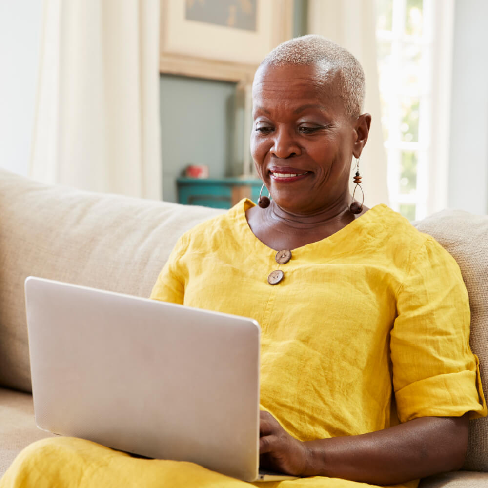 Smiling older woman in a yellow top browsing on a laptop at home with fiber internet