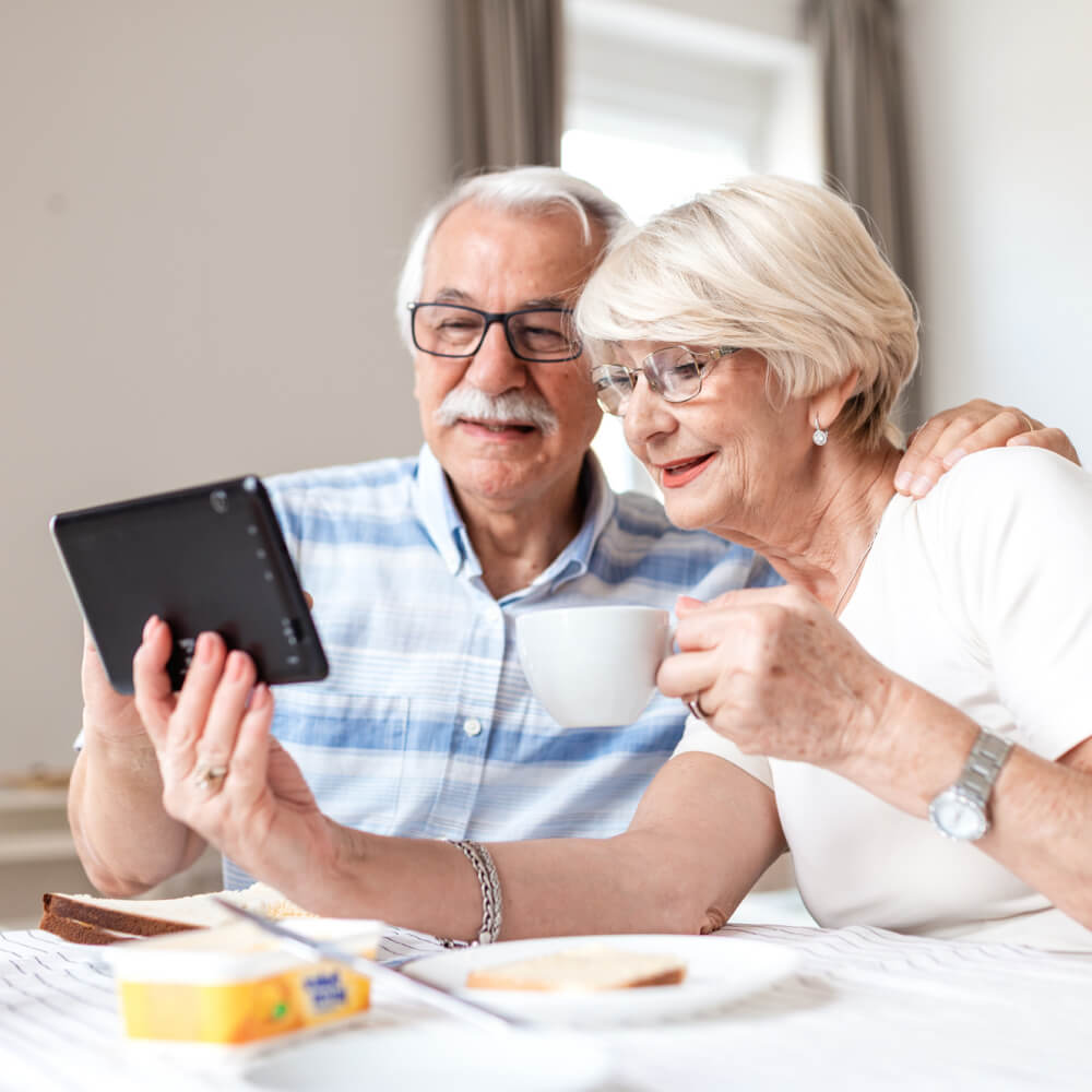 Smiling older couple at a breakfast table looking at a tablet together over coffee