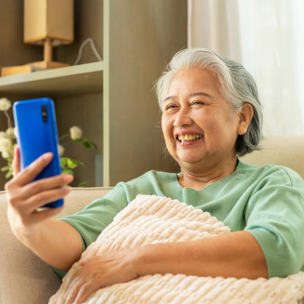 Laughing older woman on a sofa holding up a smartphone during a video call
