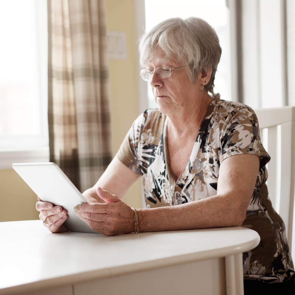 Older woman with glasses at a table checking her internet speed on a tablet