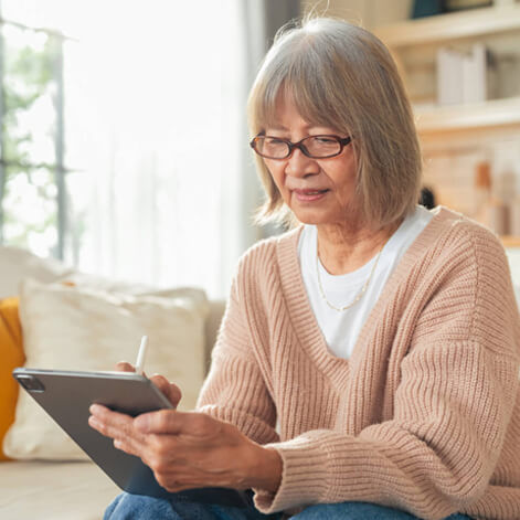 A senior woman in a cozy cardigan sketches on her tablet at home, connected and at ease.