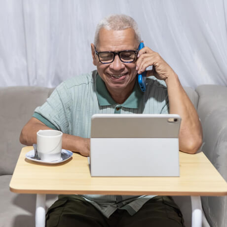 A senior man talks on the phone with a provider while comparing plans on his tablet at home
