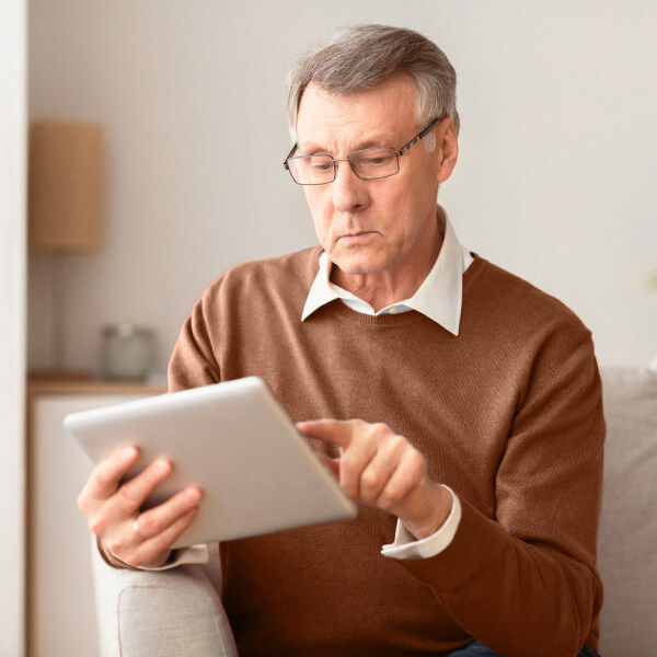 Older man with glasses in a brown sweater browsing on a tablet at home