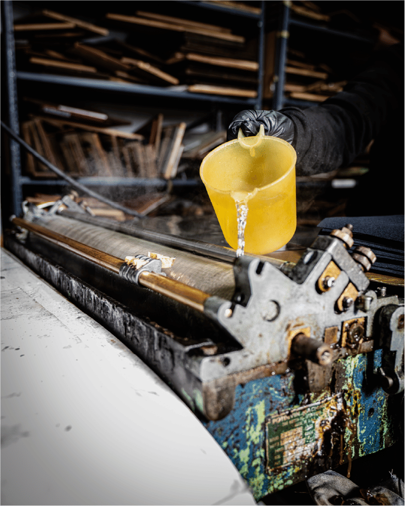 Gloved hand pouring liquid onto industrial printing machine surface