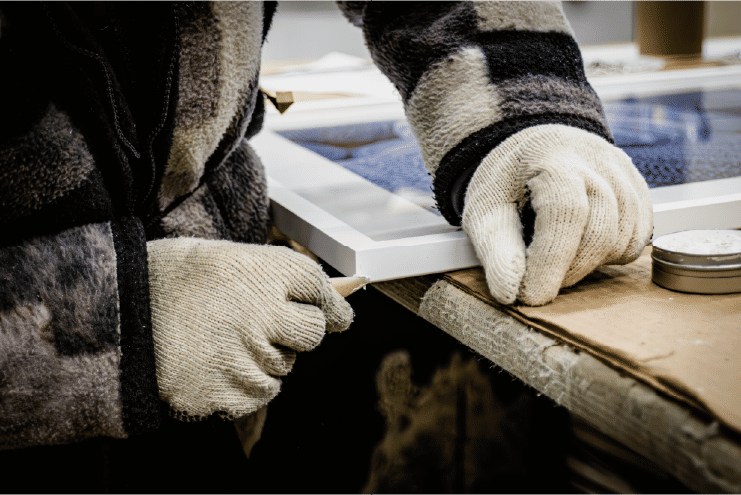 Gloved worker handling framed artwork on workbench