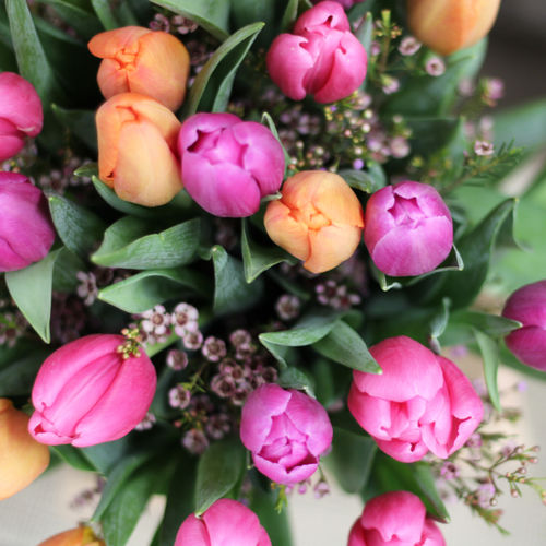 Rosa och oranga blommor blandat med gröna blad i en bukett på en bild tagen ovanifrån