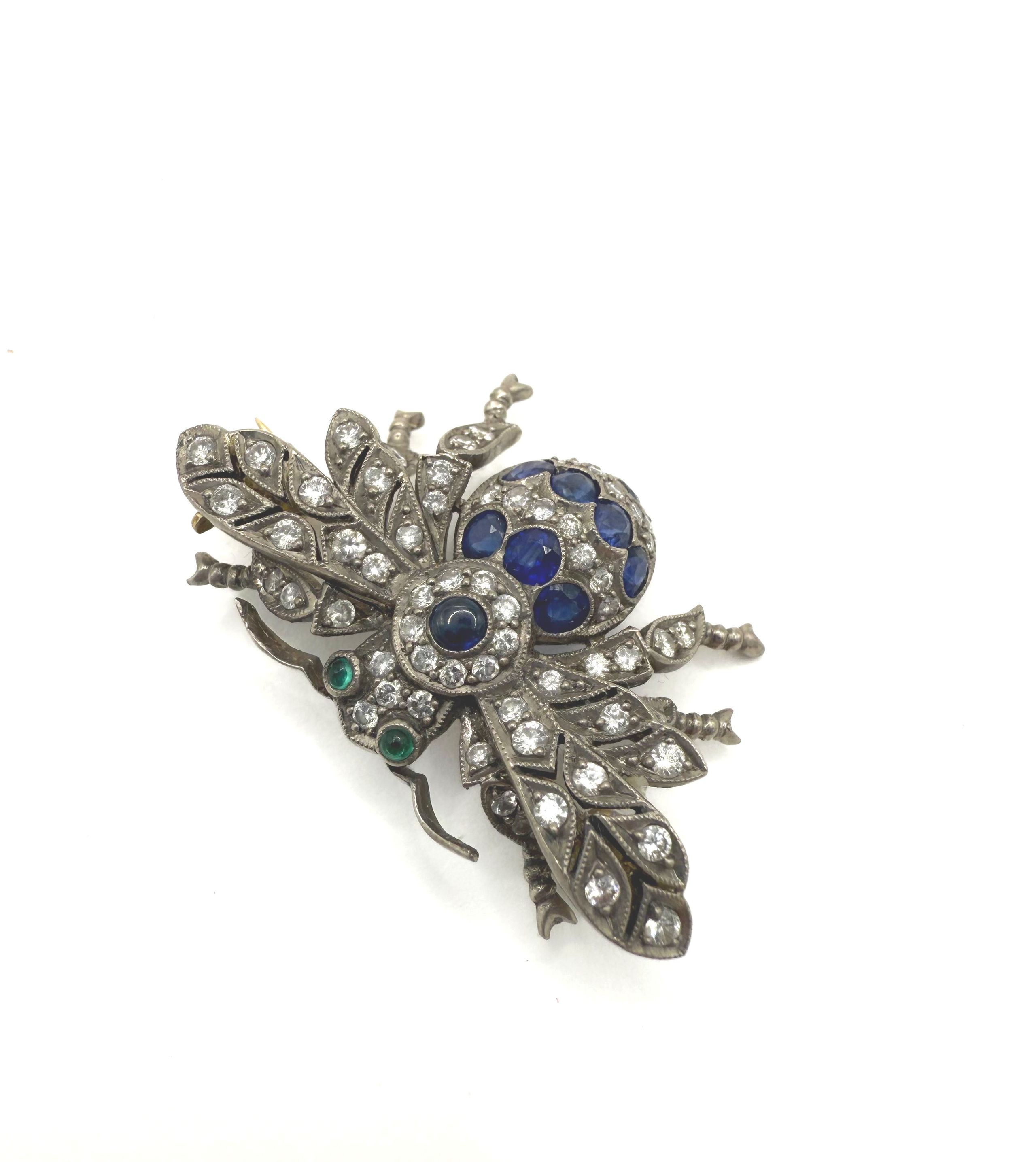 Broche abeille en or gris et jaune (750 millièmes) ornée de saphirs et diamants ronds, les yeux ornés d’émeraudes cabochons. - Lazuli