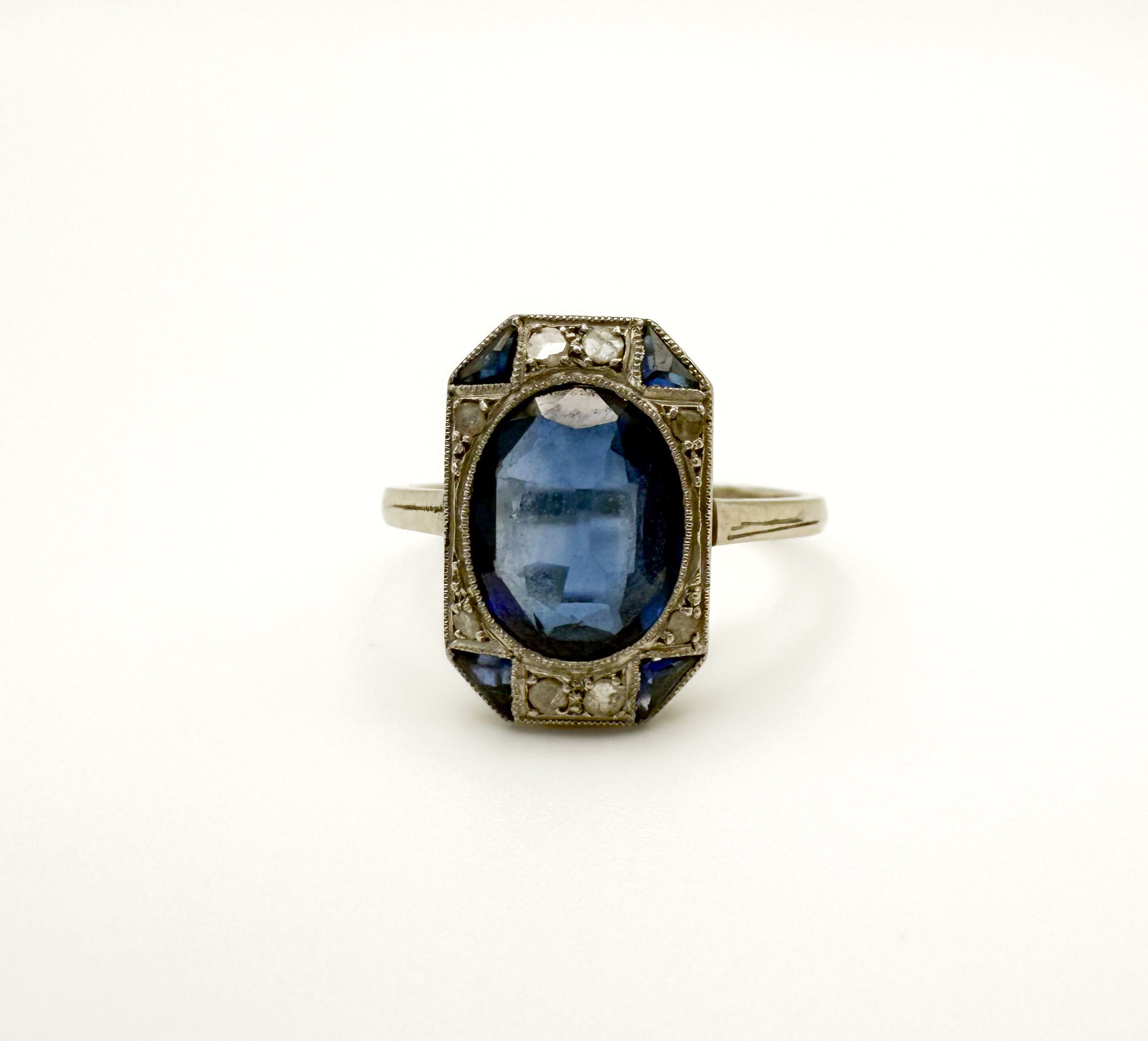 Bague en gris (750 millèmes) et platine ornée d’un saphir synthétique ovale dans un entourage de diamants taillés en rose et saphirs calibrés. - Lazuli