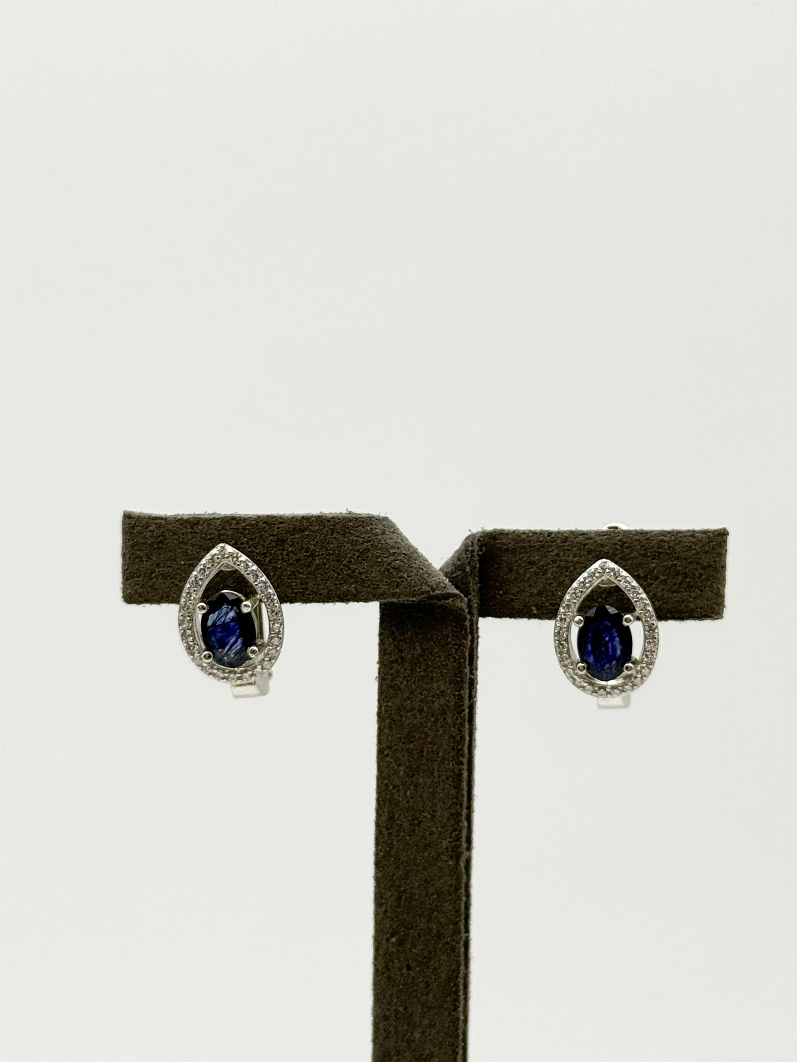 Paire de clous d&rsquo;oreilles en argent (925 millième) ornés chacun d&rsquo;un saphir ovale (traité) dans un entourage de pierres blanches rondes. - Lazuli