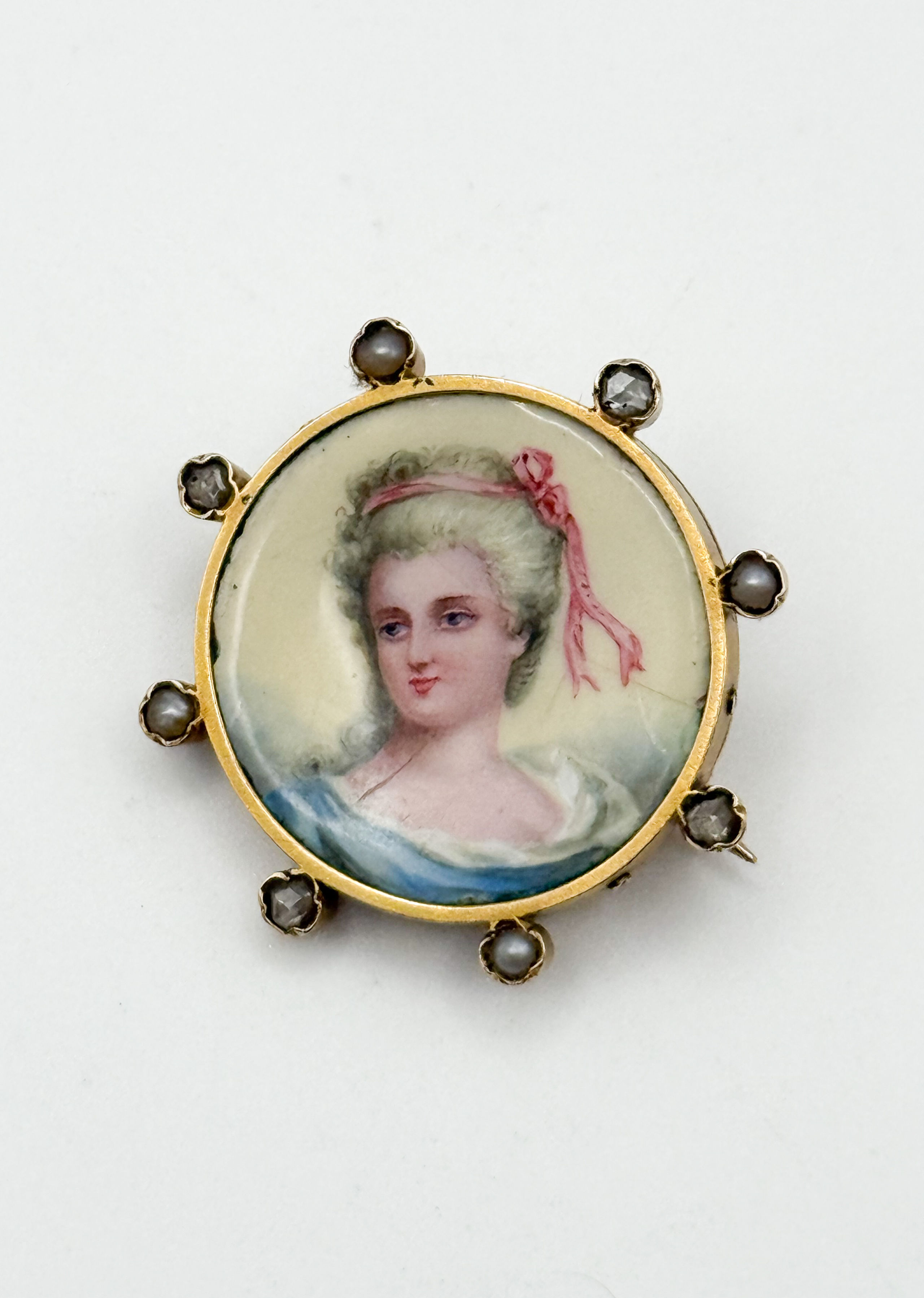 Broche ronde en or jaune (750 millièmes) ornée d&rsquo;une miniature en porcelaine représentant le portrait d&rsquo;une élégante polychromé, dans un entourage alternant diamants taille ancienne et perles. - Lazuli