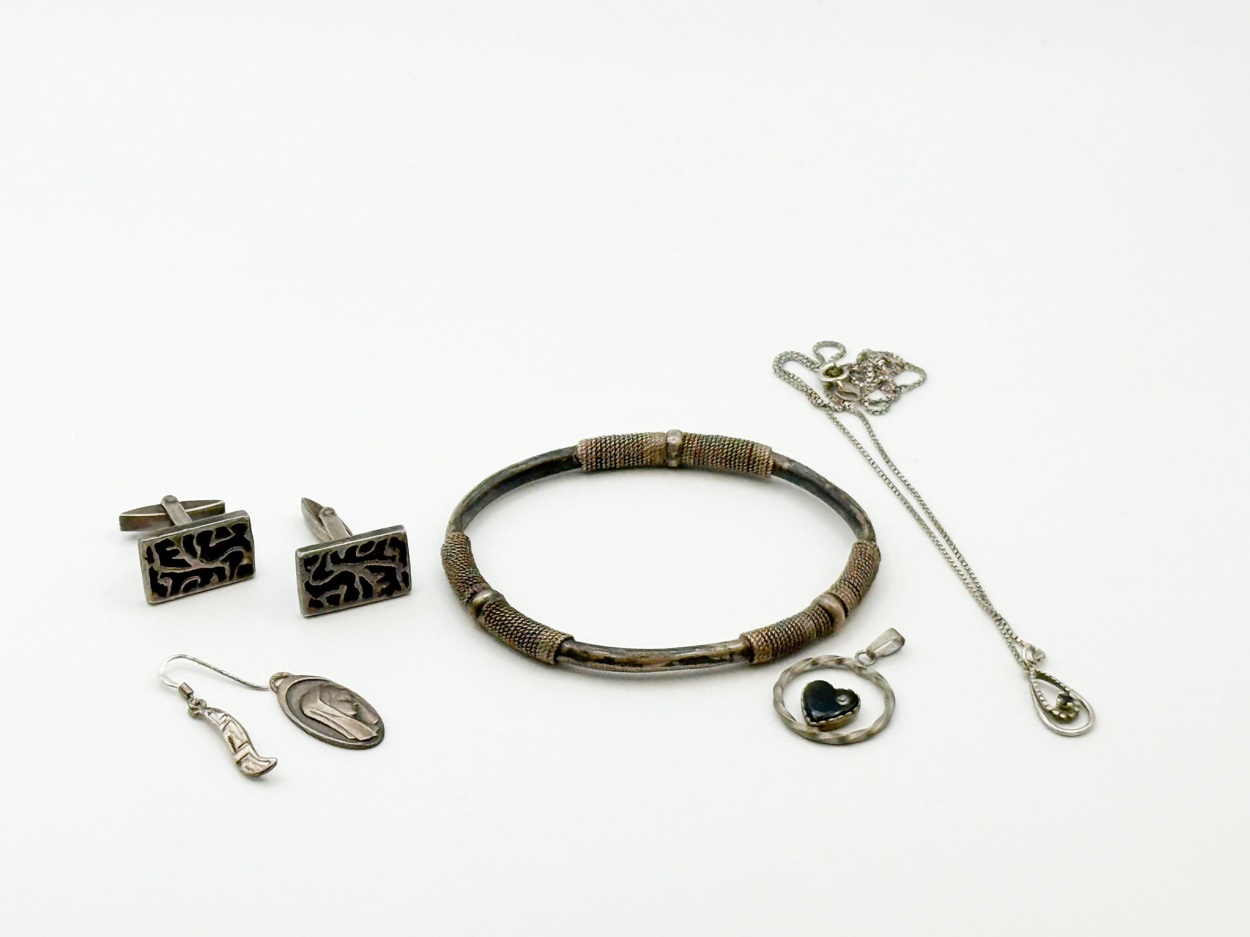 Lot d&rsquo;argent comprenant un jonc, une chaîne et un pendentif goutte, un pendant d&rsquo;oreille, une paire de boutons de manchettes et un pendentif ovale religieux. - Lazuli