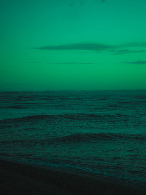 A calm sea under a low horizon, the whole frame washed in an unnatural emerald green with a thin bar of cloud at the skyline