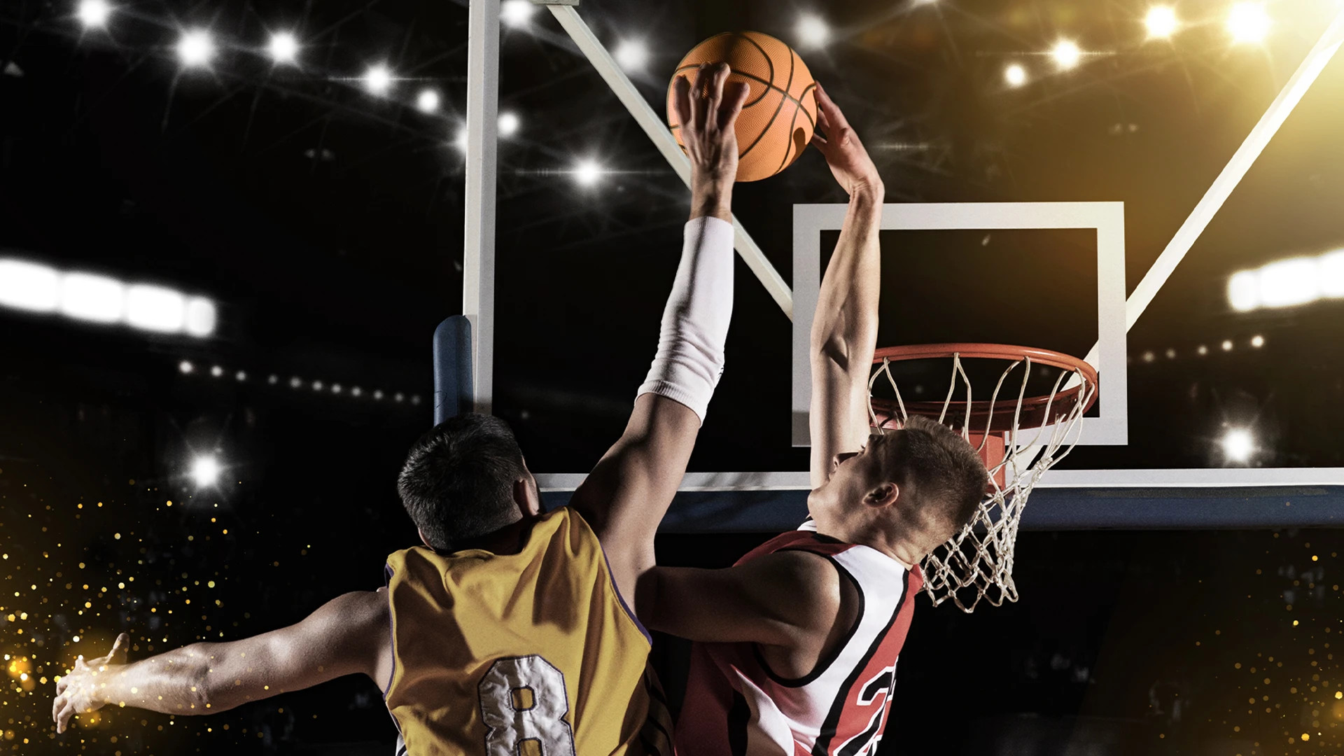 Två basketspelare som spelar basket. En spelare dunkar bollen i nät och den andar spelaren försöker försvara