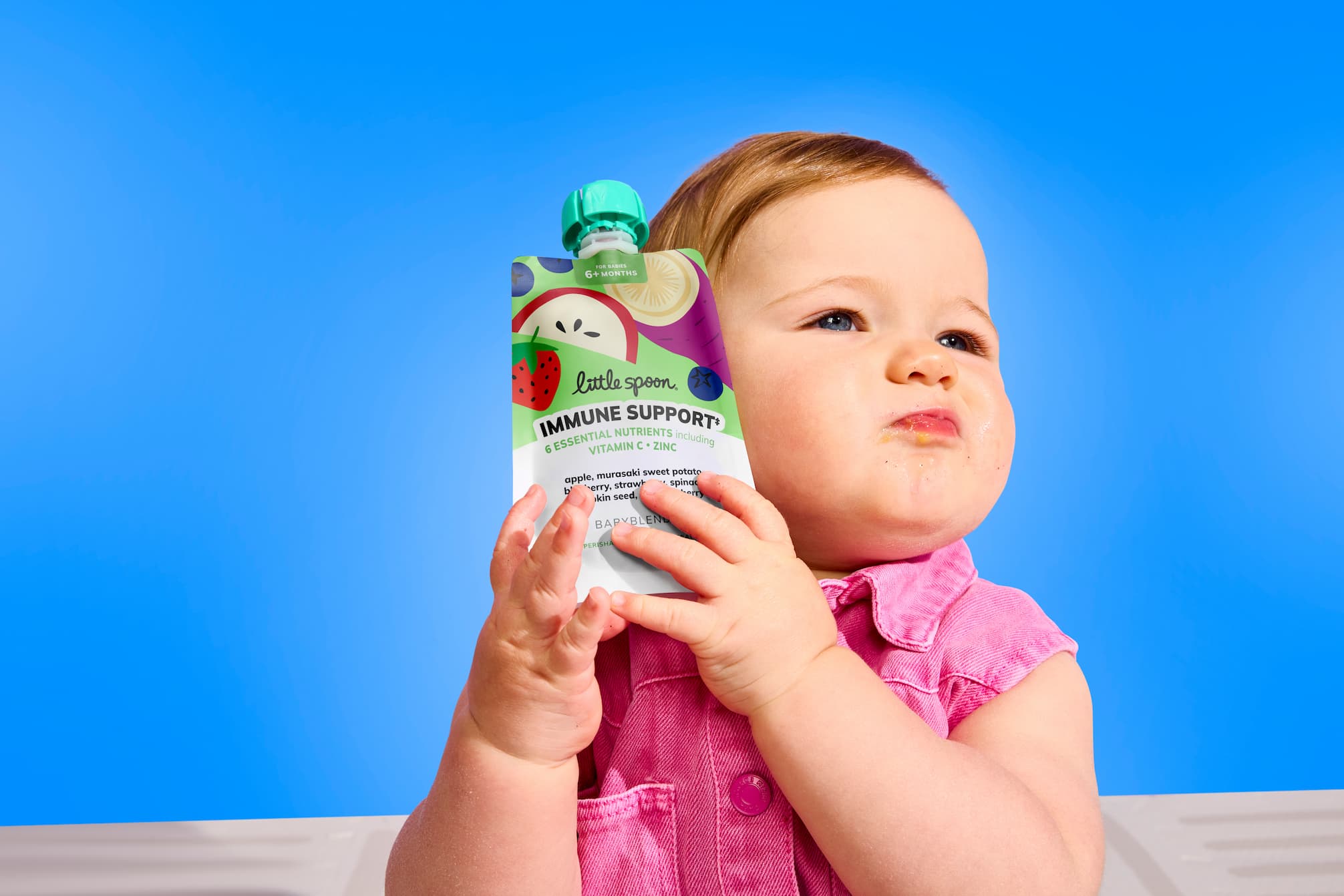 Baby holding a Little Spoon Babyblends+ pouch with immune support formula.
