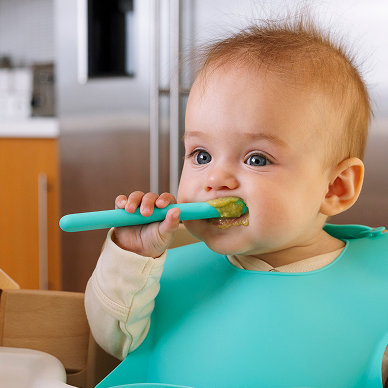 Photo of Baby eating puree food with blue silicone spoon and bib.