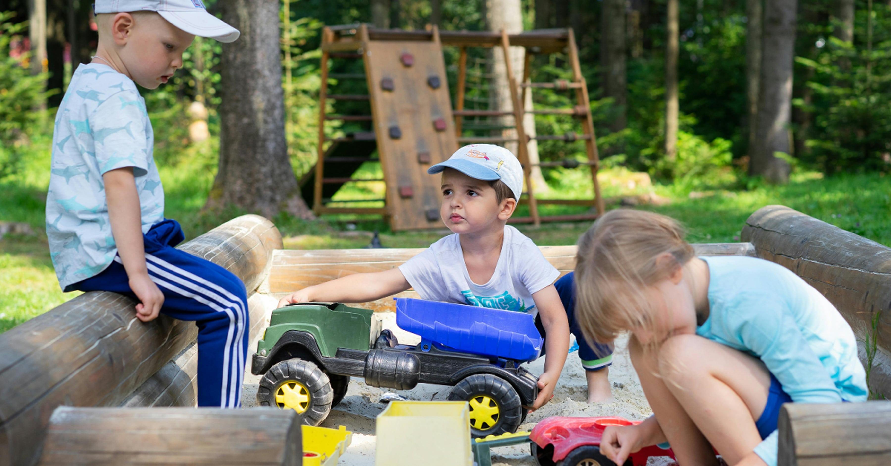 Young children playing with toy trucks in a wooden sandbox.