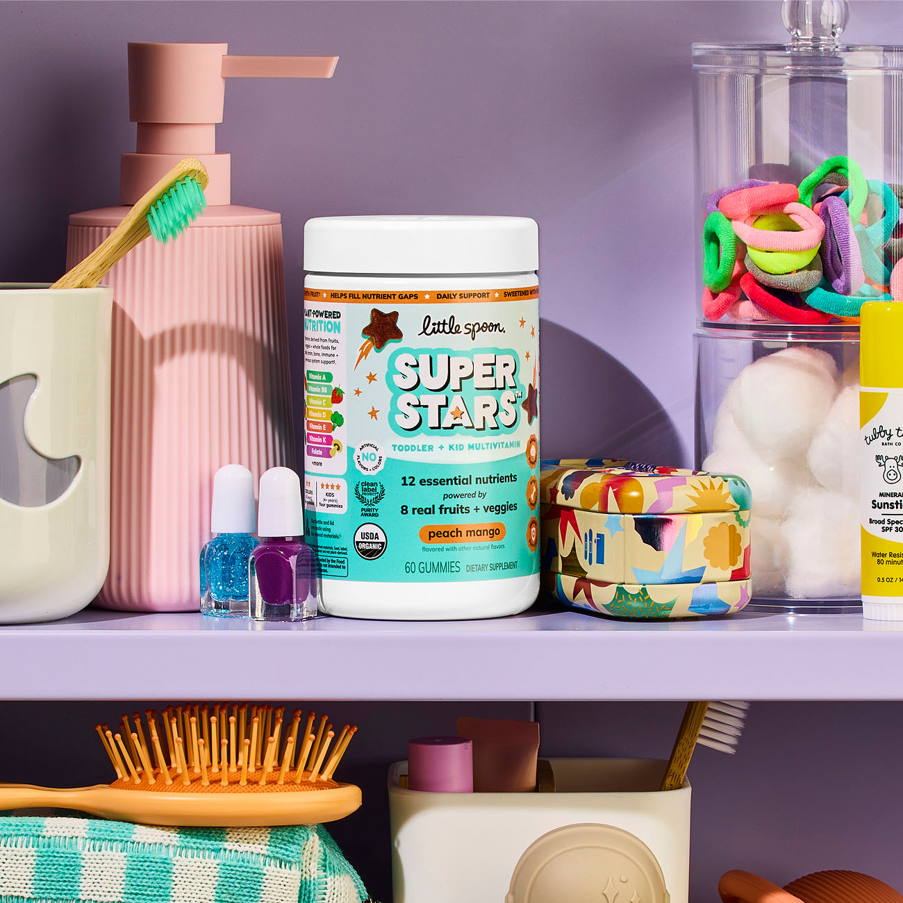 Peach Mango Superstars Multivitamin jar on a shelf with nail polish, hair ties, tooth brush, hair brush, soap, cotton balls