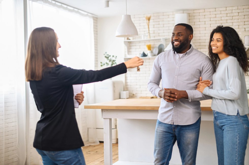 Relocation concept. A smiling cheerful multiracial couple receives the keys to a new home from a real estate agent, smiling African man and woman rent new apartment header image